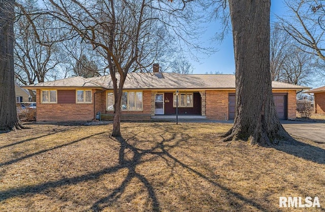 single story home with driveway, an attached garage, a chimney, a front lawn, and brick siding