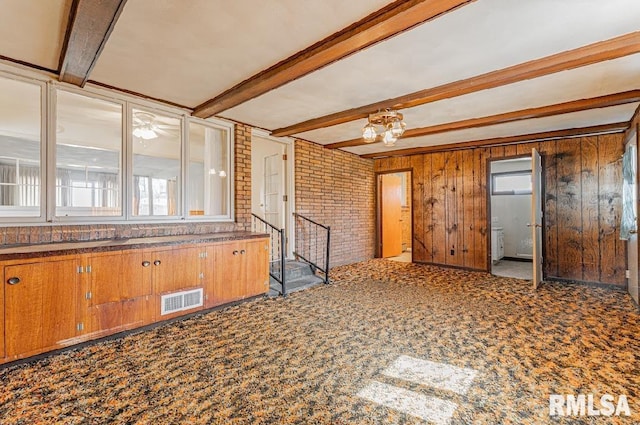 interior space with visible vents, brown cabinets, beamed ceiling, wood walls, and brick wall