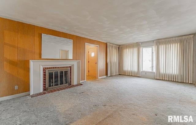 unfurnished living room featuring wooden walls, a brick fireplace, crown molding, and carpet floors