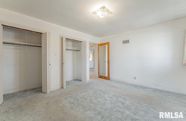 unfurnished bedroom with visible vents, multiple closets, and carpet