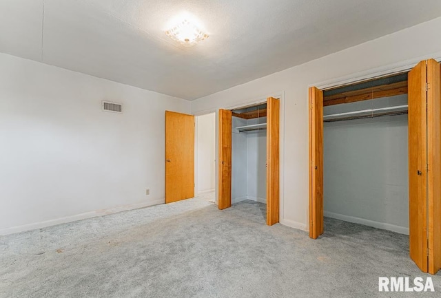 unfurnished bedroom with visible vents, carpet flooring, two closets, and baseboards