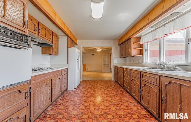 kitchen featuring wallpapered walls, white appliances, brown cabinets, and a sink