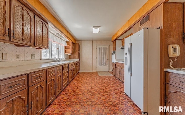 kitchen with visible vents, wallpapered walls, light countertops, brown cabinets, and white appliances