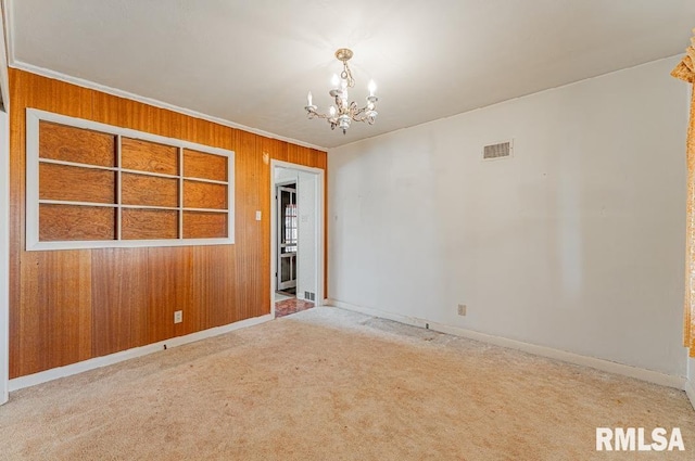 empty room with visible vents, carpet, wood walls, ornamental molding, and an inviting chandelier