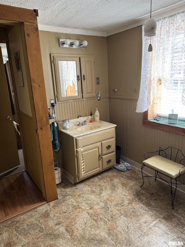 bathroom with a wainscoted wall, a textured ceiling, a healthy amount of sunlight, and vanity