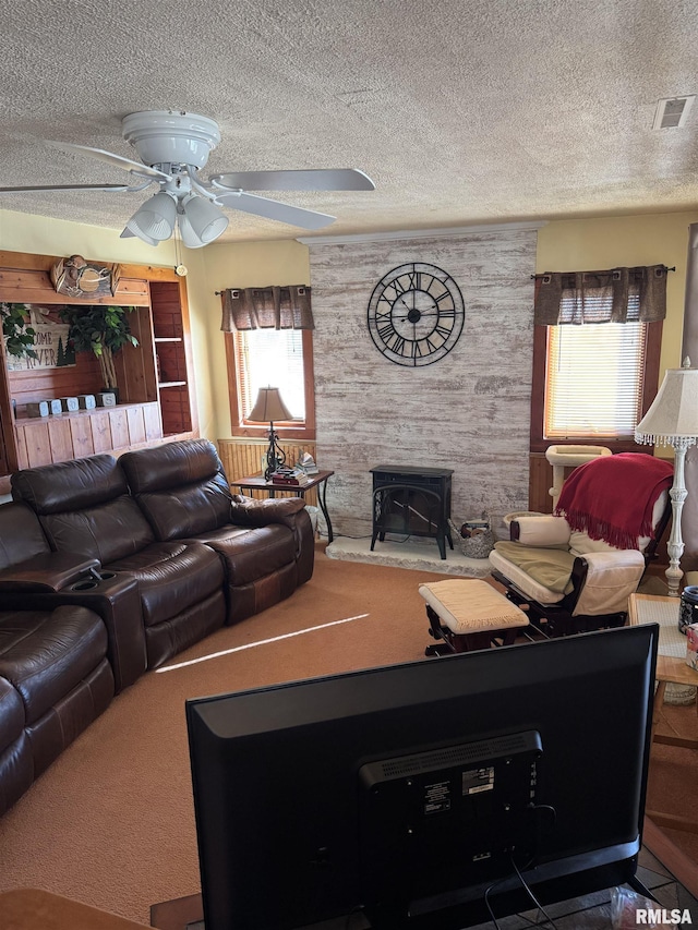 carpeted living area featuring a wood stove, a ceiling fan, visible vents, and a textured ceiling