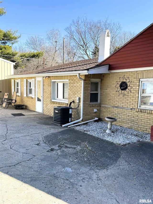 back of house featuring cooling unit, a patio, brick siding, and a chimney