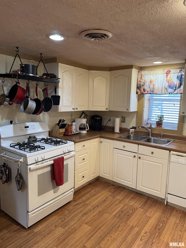 kitchen with white appliances, visible vents, a sink, light wood-style floors, and white cabinetry