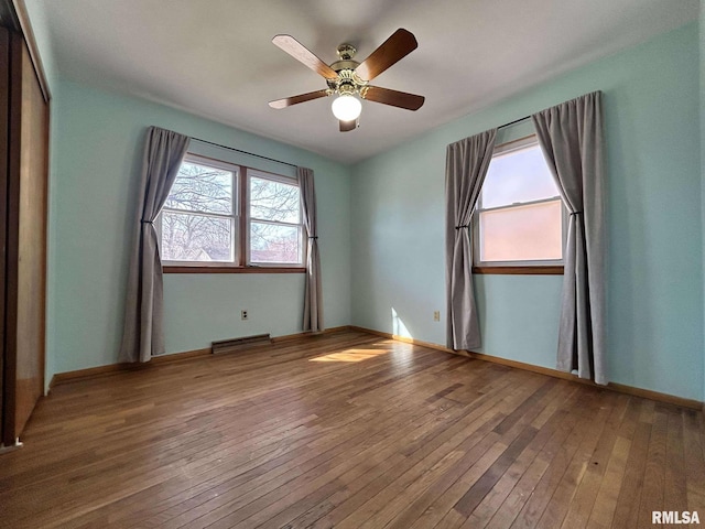 empty room featuring visible vents, wood-type flooring, baseboards, and a ceiling fan