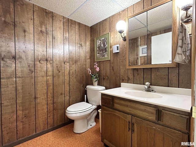 half bath featuring vanity, toilet, a paneled ceiling, and wood walls