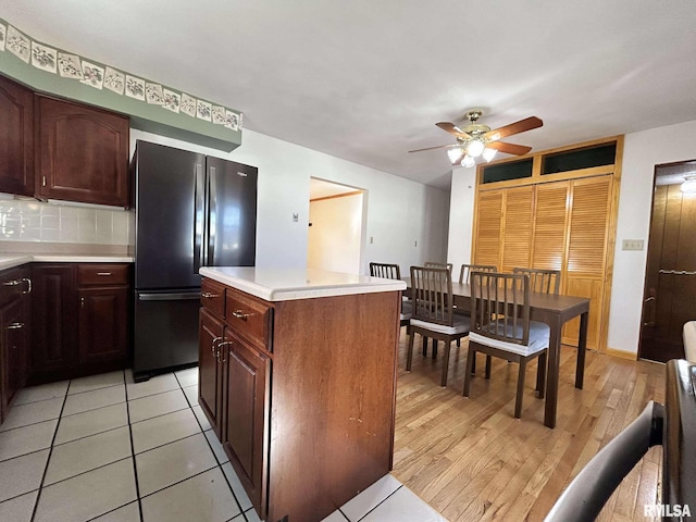 kitchen with backsplash, a center island, light countertops, freestanding refrigerator, and a ceiling fan