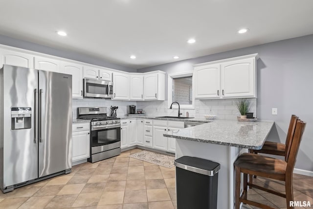 kitchen featuring a sink, stainless steel appliances, a peninsula, a breakfast bar area, and light stone countertops