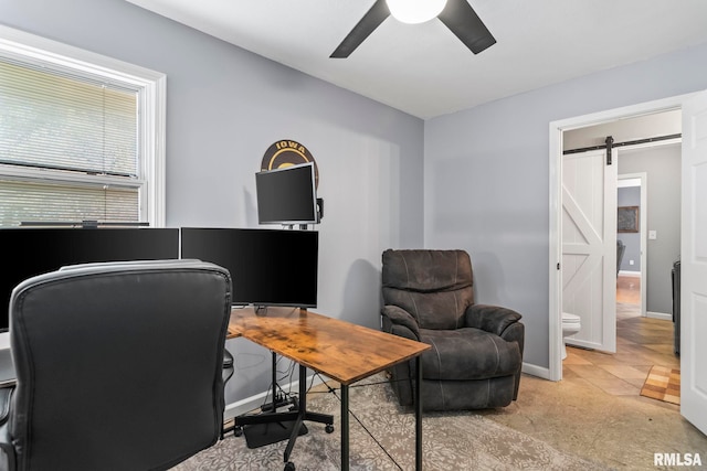 office area featuring baseboards, a ceiling fan, and a barn door