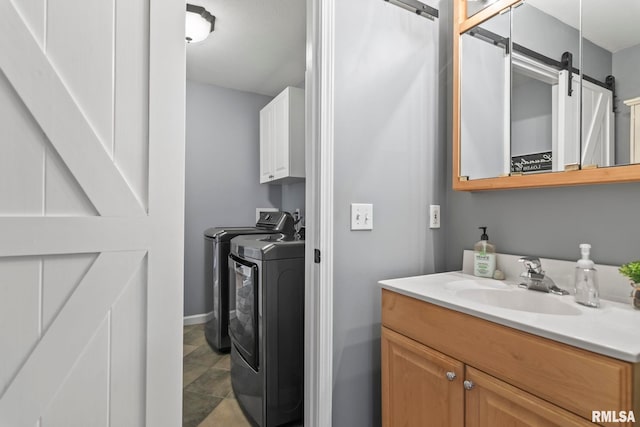 clothes washing area featuring washer and clothes dryer, a sink, a barn door, cabinet space, and baseboards