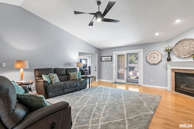 living room featuring a tiled fireplace, vaulted ceiling, wood finished floors, and baseboards