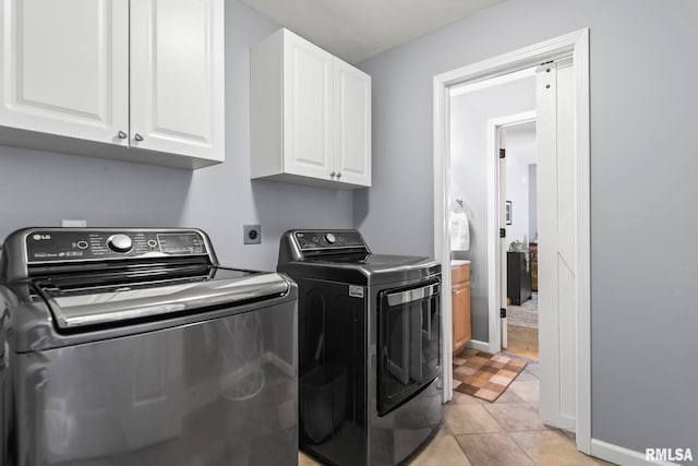 laundry room with light tile patterned floors, cabinet space, baseboards, and washing machine and clothes dryer