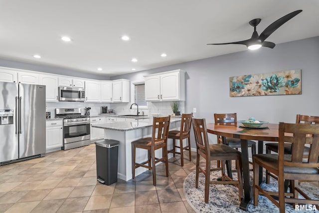 kitchen with light stone counters, decorative backsplash, white cabinets, stainless steel appliances, and a sink