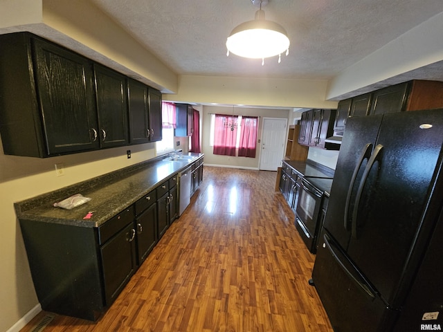 kitchen featuring wood finished floors, a sink, black appliances, a textured ceiling, and dark cabinets