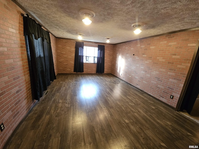 unfurnished room with dark wood-type flooring, brick wall, and a textured ceiling