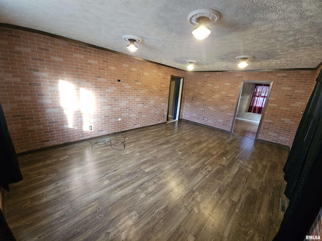 empty room featuring brick wall, a textured ceiling, and wood finished floors