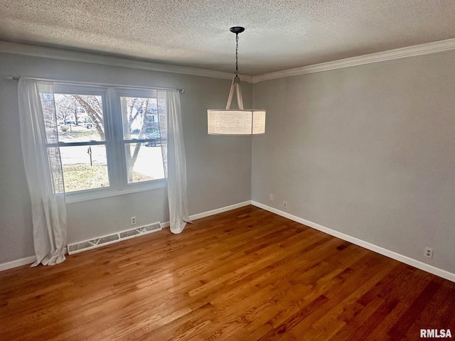 unfurnished dining area with crown molding, wood finished floors, baseboards, and a textured ceiling