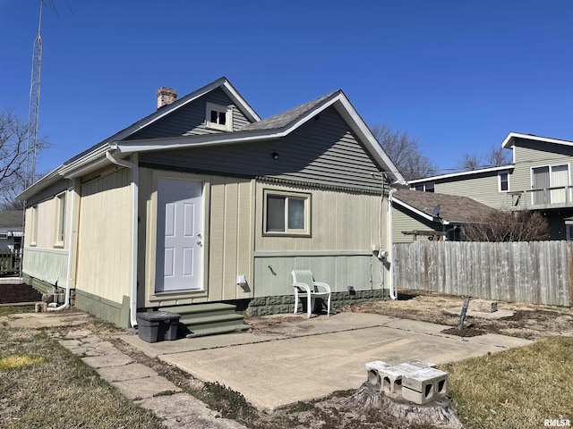 rear view of property with entry steps, a patio, fence, and a chimney