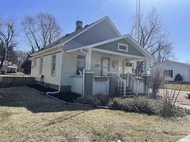 bungalow with a front lawn, covered porch, and a chimney