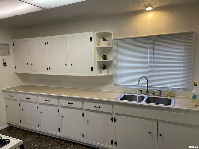 kitchen featuring a sink, a drop ceiling, open shelves, white cabinetry, and light countertops