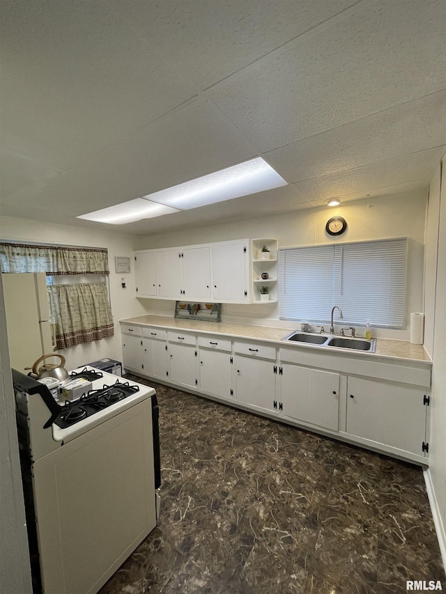 kitchen with light countertops, range with gas stovetop, marble finish floor, white cabinetry, and a sink