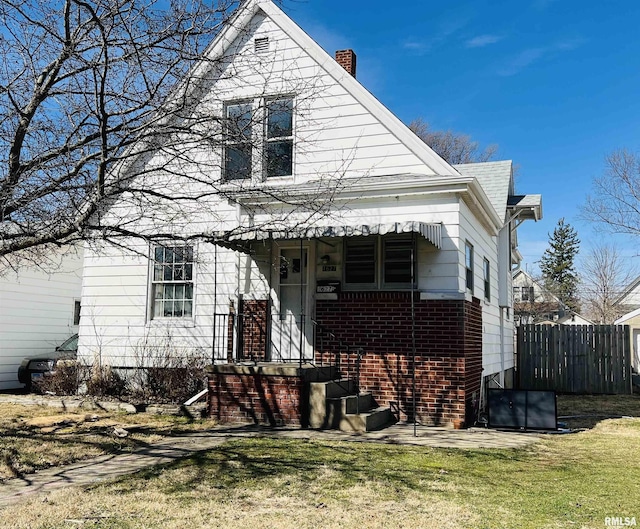 view of front of house with brick siding, a chimney, a front lawn, and fence