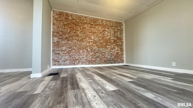 unfurnished room featuring visible vents, wood finished floors, baseboards, and brick wall