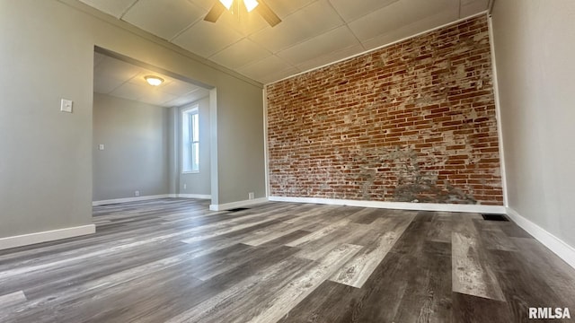 empty room with ceiling fan, baseboards, wood finished floors, and brick wall