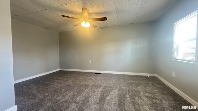 unfurnished room featuring a drop ceiling, ceiling fan, baseboards, and dark colored carpet