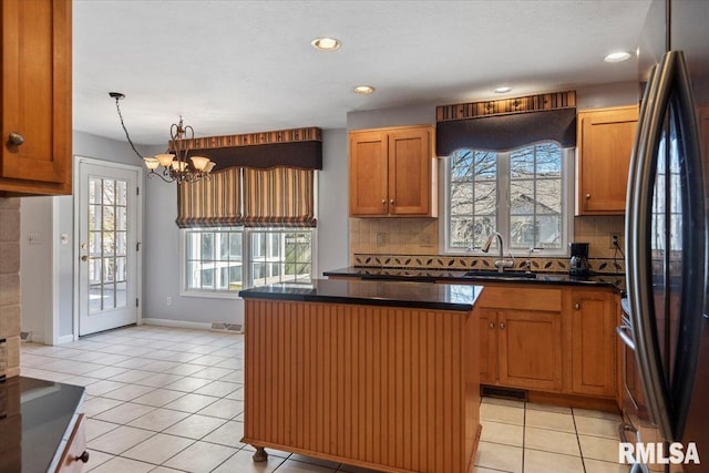 kitchen featuring dark countertops, refrigerator, light tile patterned floors, and a sink