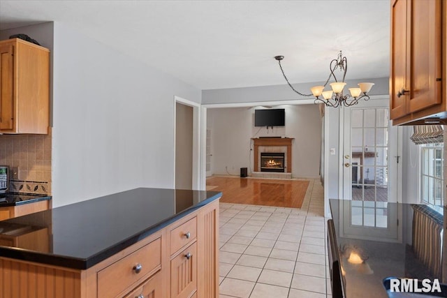 kitchen with dark countertops, light tile patterned floors, decorative backsplash, a fireplace, and an inviting chandelier