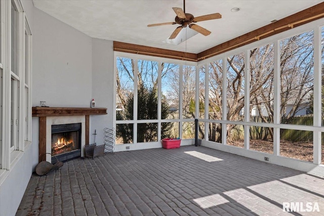 unfurnished sunroom with a warm lit fireplace and ceiling fan