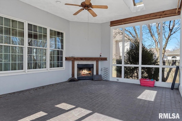 unfurnished sunroom featuring ceiling fan, a skylight, and a lit fireplace