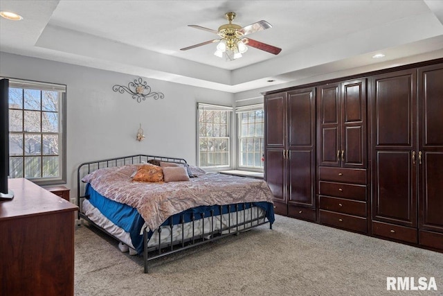 bedroom featuring a tray ceiling, multiple windows, light colored carpet, and ceiling fan