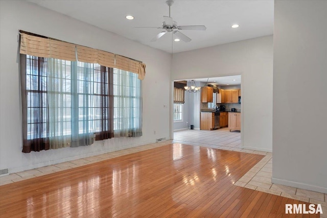 unfurnished living room with visible vents, ceiling fan with notable chandelier, recessed lighting, light tile patterned flooring, and baseboards