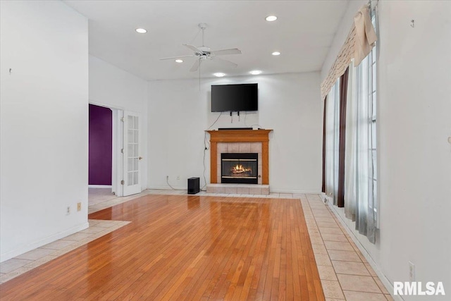 unfurnished living room with hardwood / wood-style floors, a ceiling fan, recessed lighting, a tile fireplace, and french doors