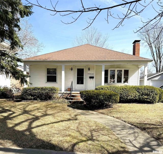 view of front of property with a porch, a chimney, a front lawn, and a shingled roof