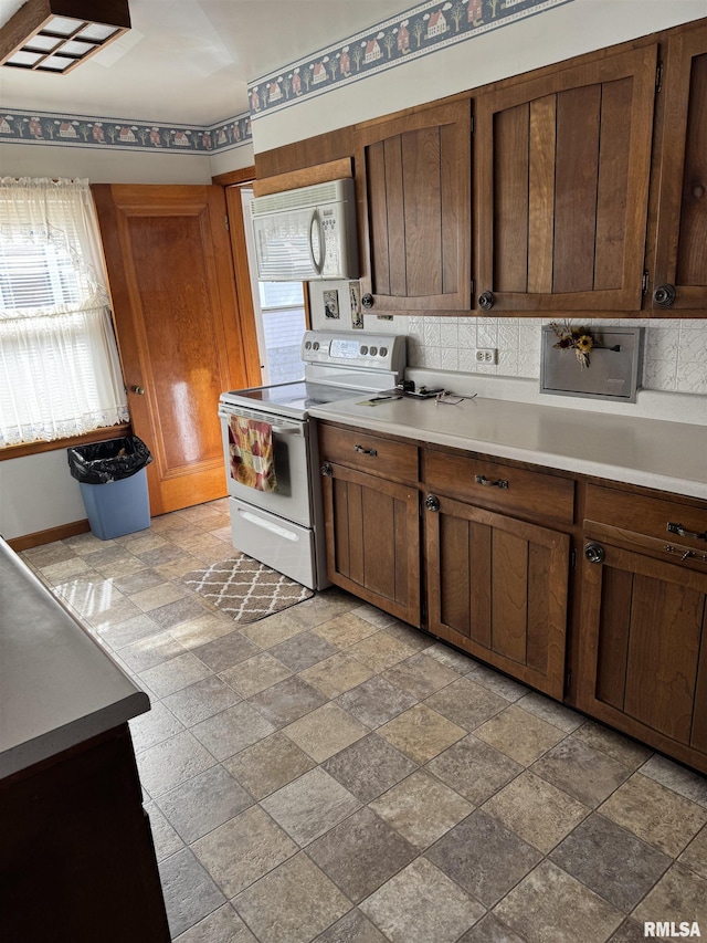 kitchen with white appliances, light countertops, backsplash, and stone finish flooring