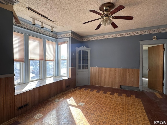 empty room featuring visible vents, wooden walls, ceiling fan, wainscoting, and a textured ceiling