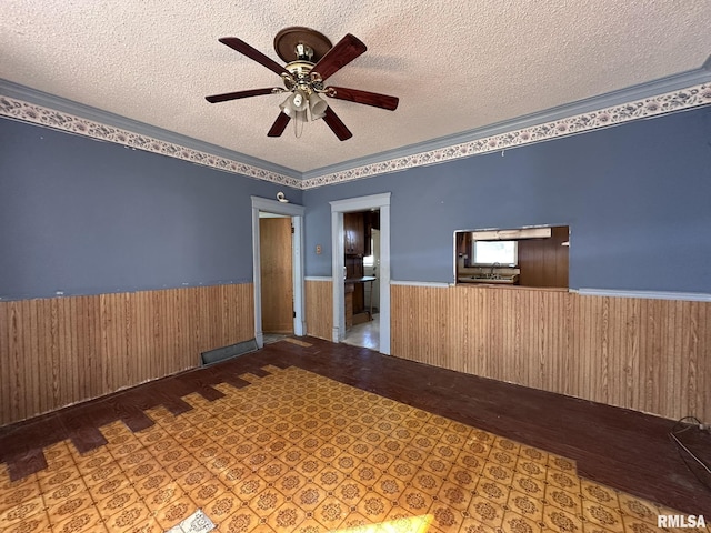 unfurnished room featuring a wainscoted wall, wood walls, a textured ceiling, and a ceiling fan