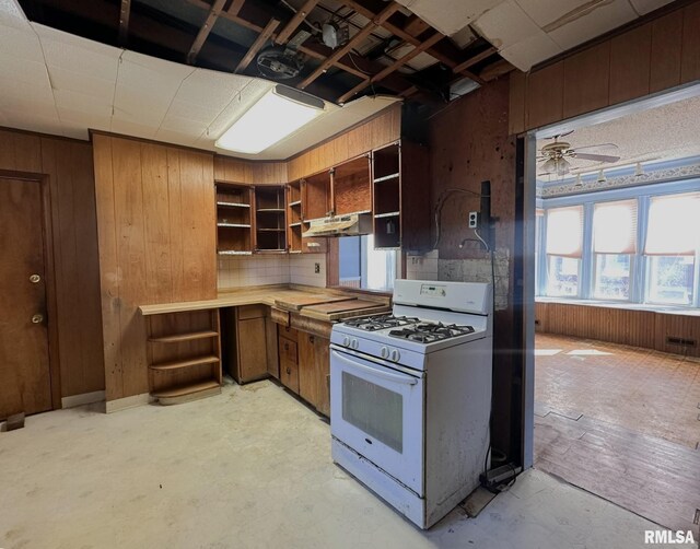 kitchen featuring open shelves, white range with gas stovetop, under cabinet range hood, and wood walls