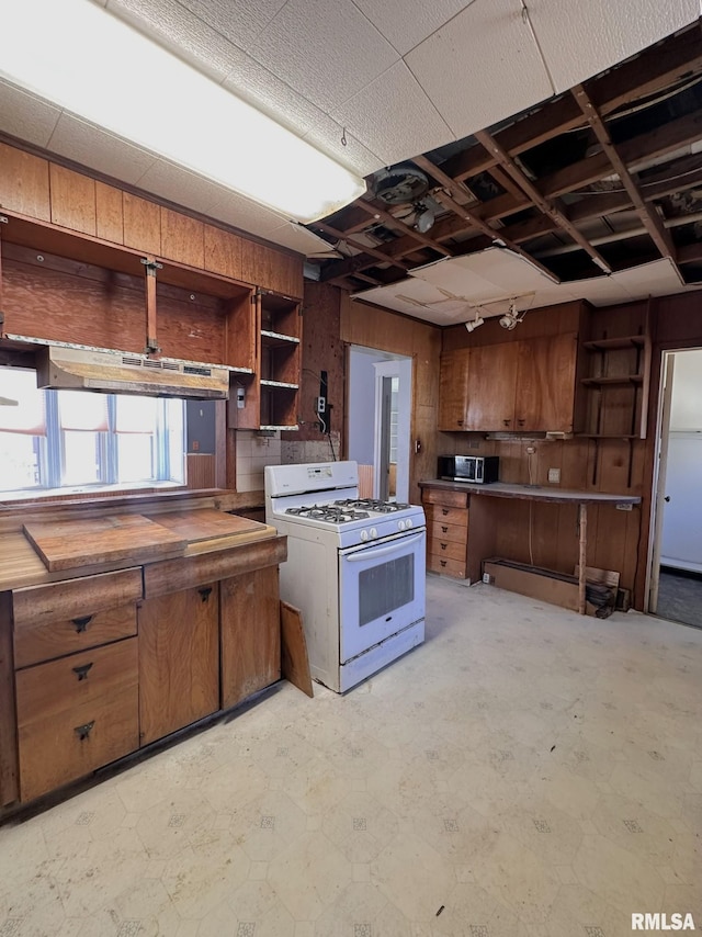 kitchen featuring open shelves, a peninsula, white range with gas stovetop, wood walls, and brown cabinets