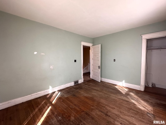 unfurnished bedroom featuring dark wood finished floors, visible vents, baseboards, and a closet