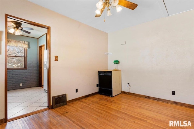 unfurnished room featuring light wood finished floors, visible vents, brick wall, baseboards, and ceiling fan