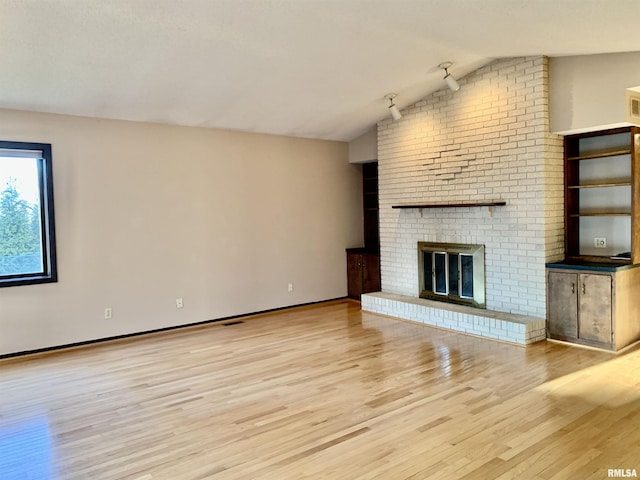 unfurnished living room with lofted ceiling, a brick fireplace, baseboards, and light wood finished floors