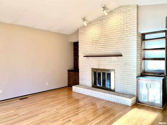 unfurnished living room featuring visible vents, a brick fireplace, wood finished floors, and vaulted ceiling